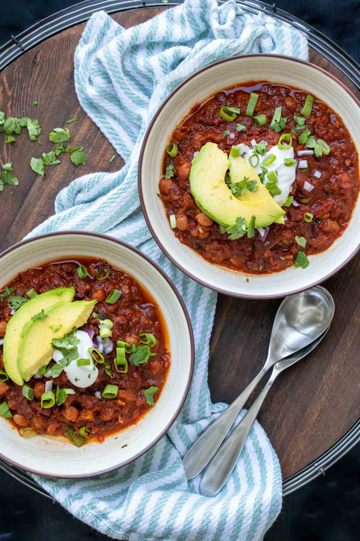 Two bowls filled with bean chili and topped with avocado slices and sour cream