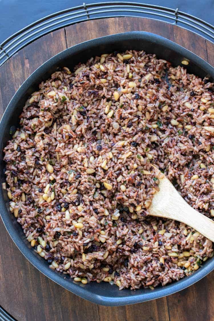 Wooden spoon mixing rice stuffing in a black pan.