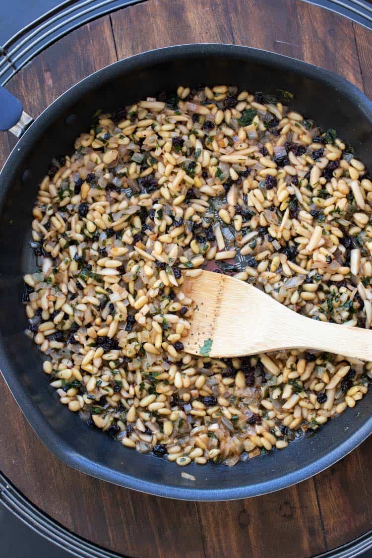 Wooden spoon mixing nuts, currants and sautéed veggies in a pan