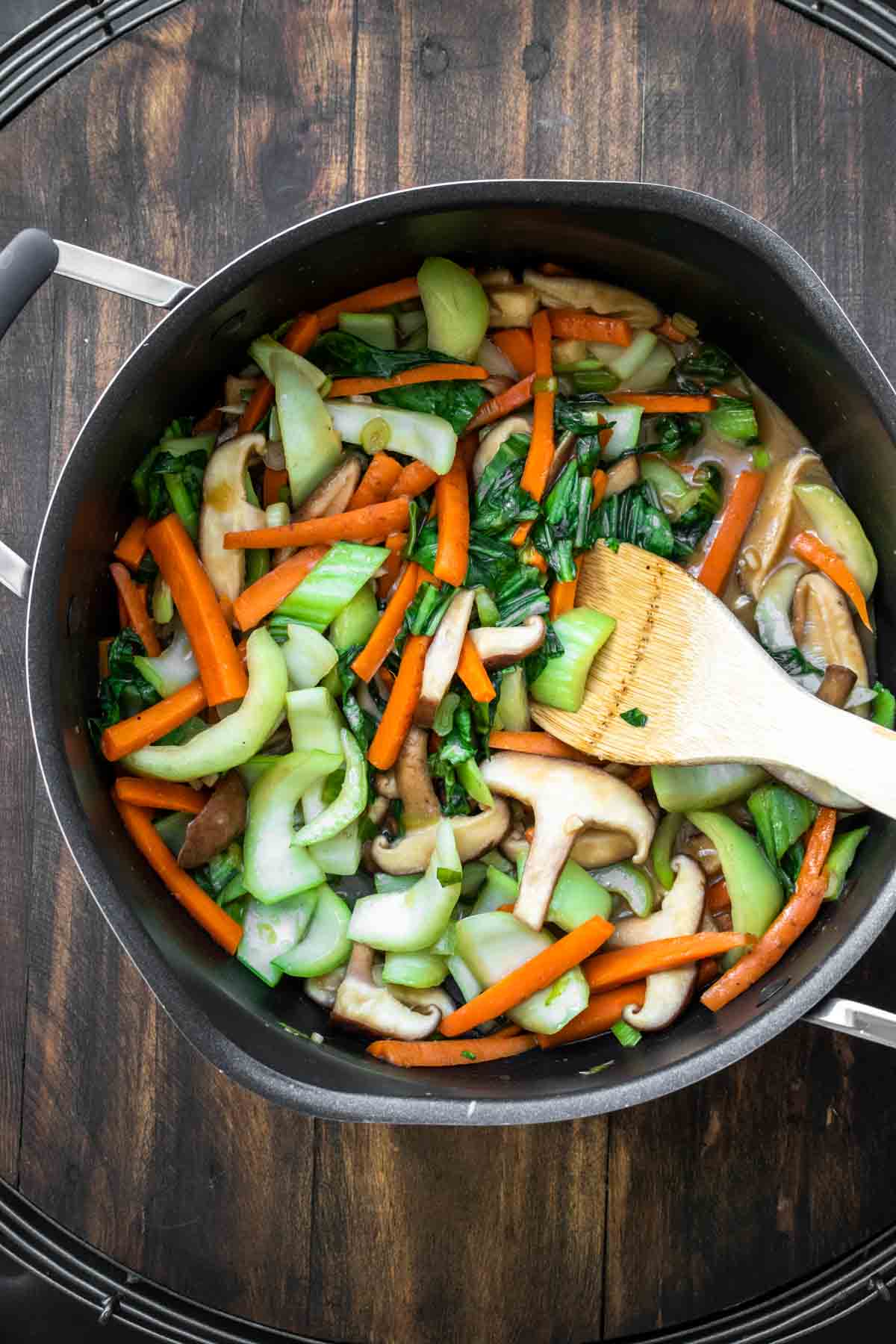 Wooden spoon stirring veggies in a pot.