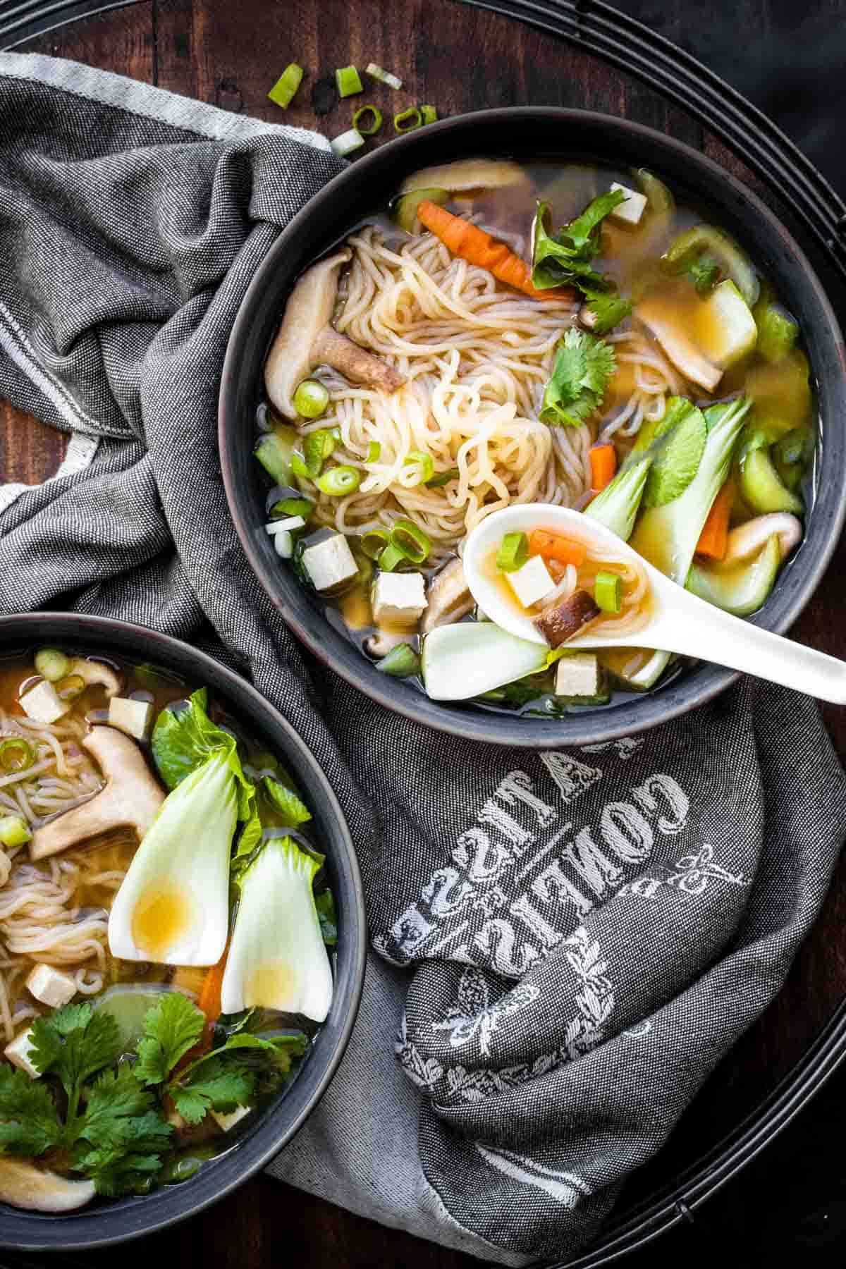 White Asian soup spoon in a bowl of veggie and noodle soup
