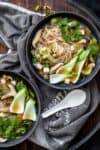 Two black bowls with a veggie and noodle based soup and a clear brown broth on a dark grey towel.