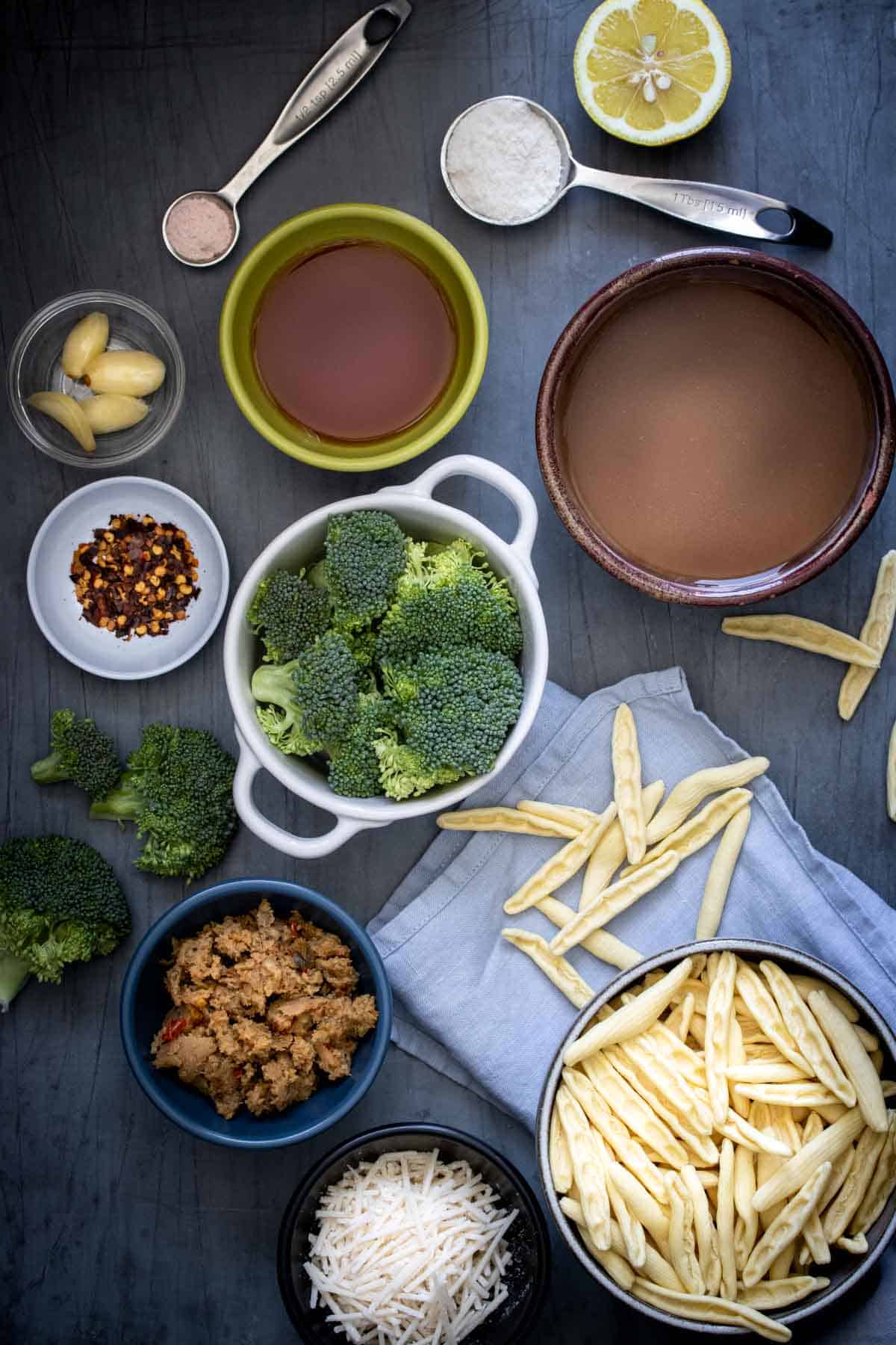 A grey background with ingredients in bowls needed to make a cavatelli and broccoli recipe