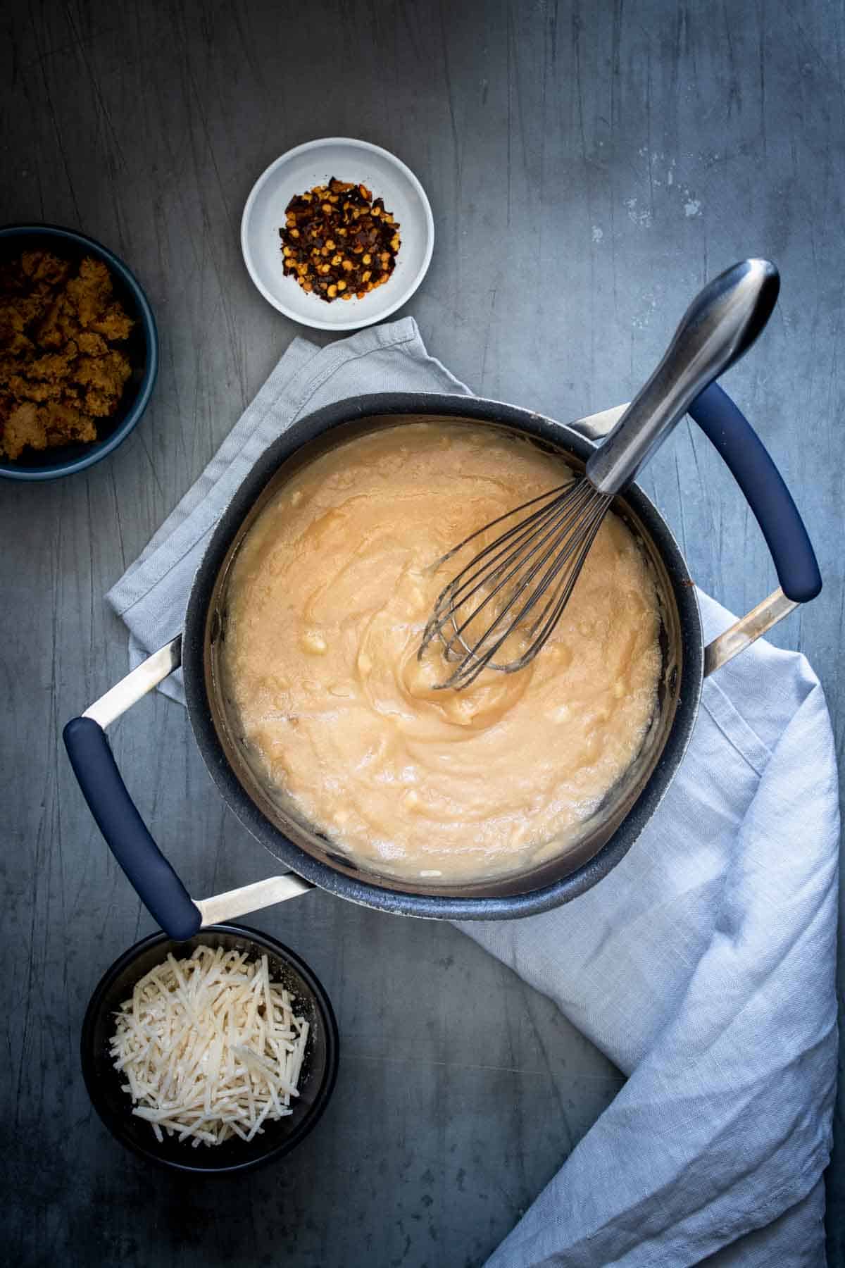 Whisk mixing a thick tan substance in a black pot