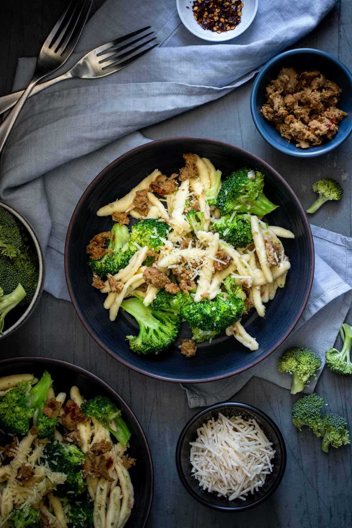 A bowl of cavatelli pasta mixed with broccoli and sausage and topped with parmesan in the light of a shadowed background