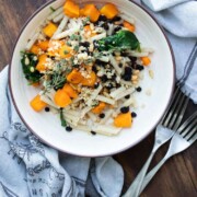 Cream plate with penne pasta, butternut squash and spinach topped with parmesan