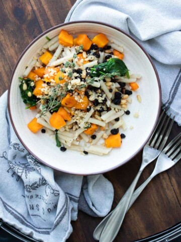 Cream plate with penne pasta, butternut squash and spinach topped with parmesan