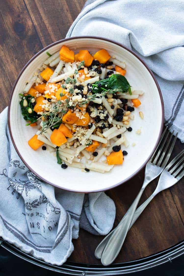 Cream plate with penne pasta, butternut squash and spinach topped with parmesan