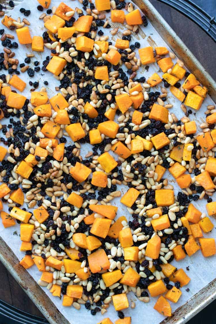 Baking sheet with pieces of cooked butternut squash, pine nuts and currants
