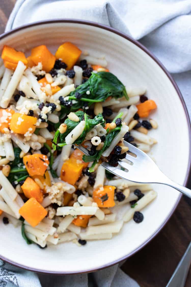 Fork taking a bite from a plate of butternut squash and spinach penne pasta