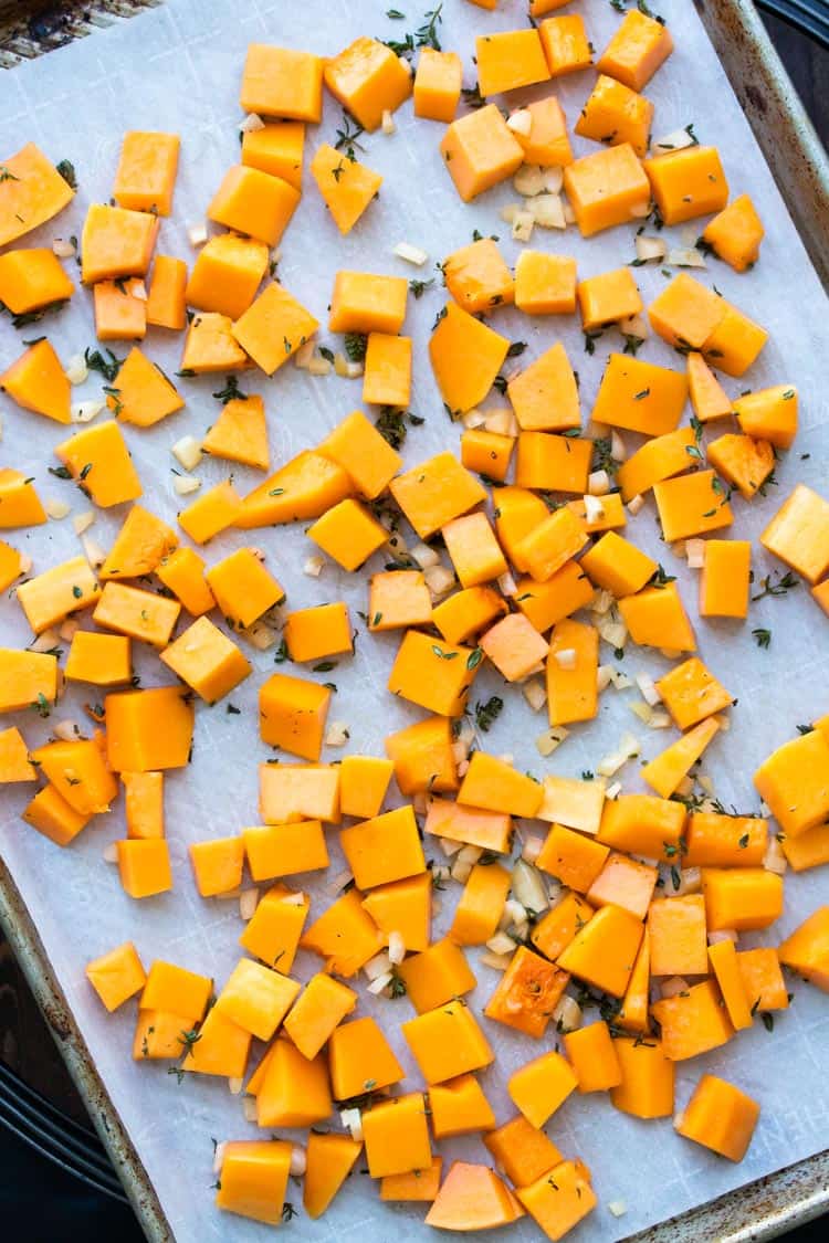 Baking sheet with parchment paper and pieces of uncooked butternut squash, thyme and garlic