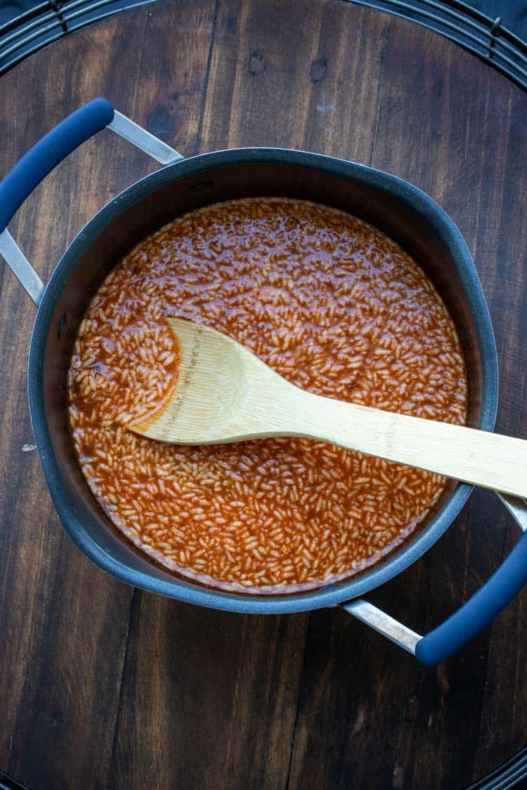 Wooden spoon stirring Mexican rice mix and water in a pot.