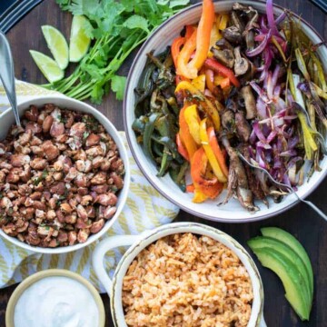 Bowls of different veggies, rice, beans and sour cream on a wooden tray
