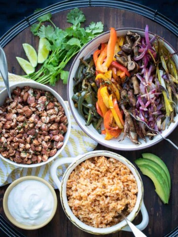 Bowls of different veggies, rice, beans and sour cream on a wooden tray