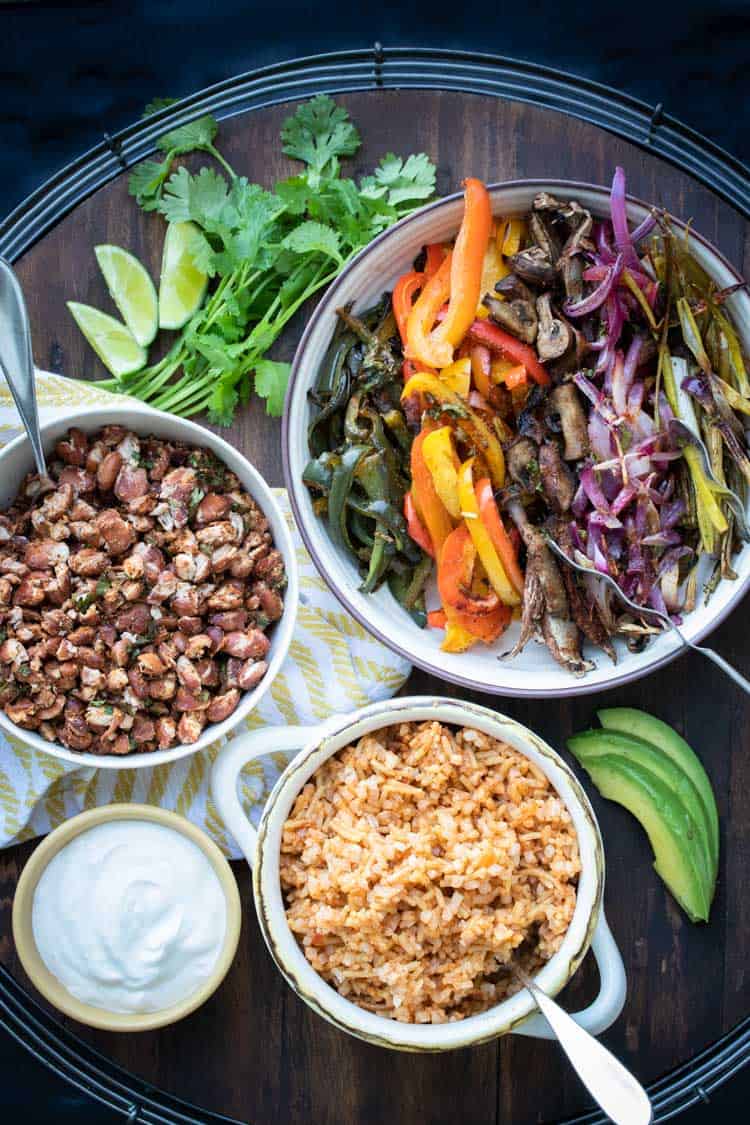 Bowls of different veggies, rice, beans and sour cream on a wooden tray