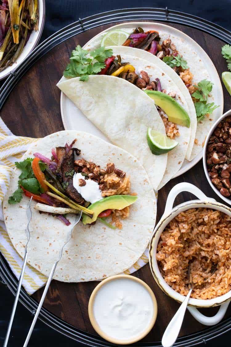 Tortillas filled with veggies, rice and beans on a wooden tray.