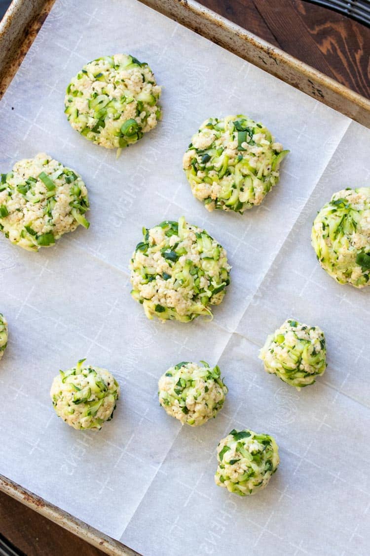 Raw zucchini fritters on a parchment lined cookie sheet