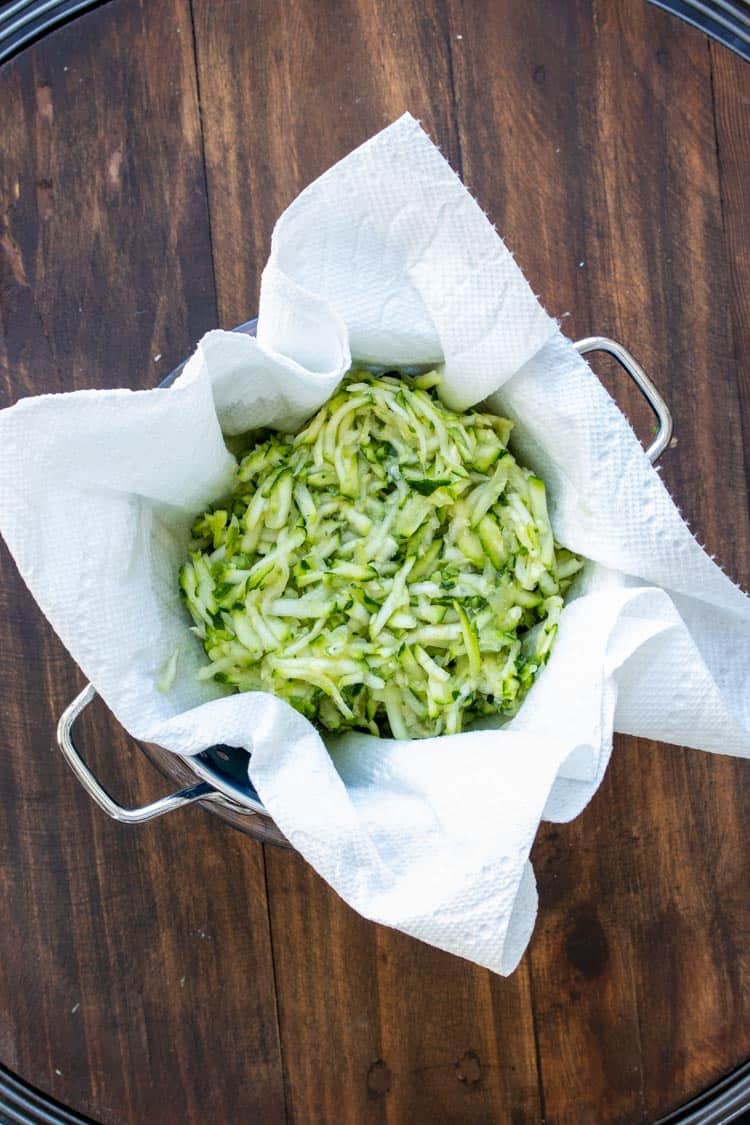 Grated zucchini on a paper towel in a strainer