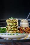 Stack of zucchini fritters drizzled with remoulade on a white plate