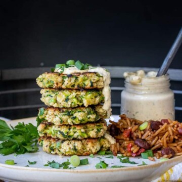 Stack of zucchini fritters drizzled with remoulade on a white plate
