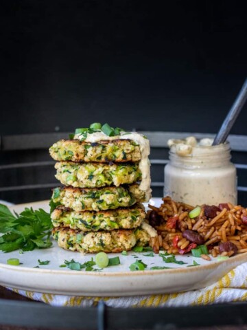 Stack of zucchini fritters drizzled with remoulade on a white plate