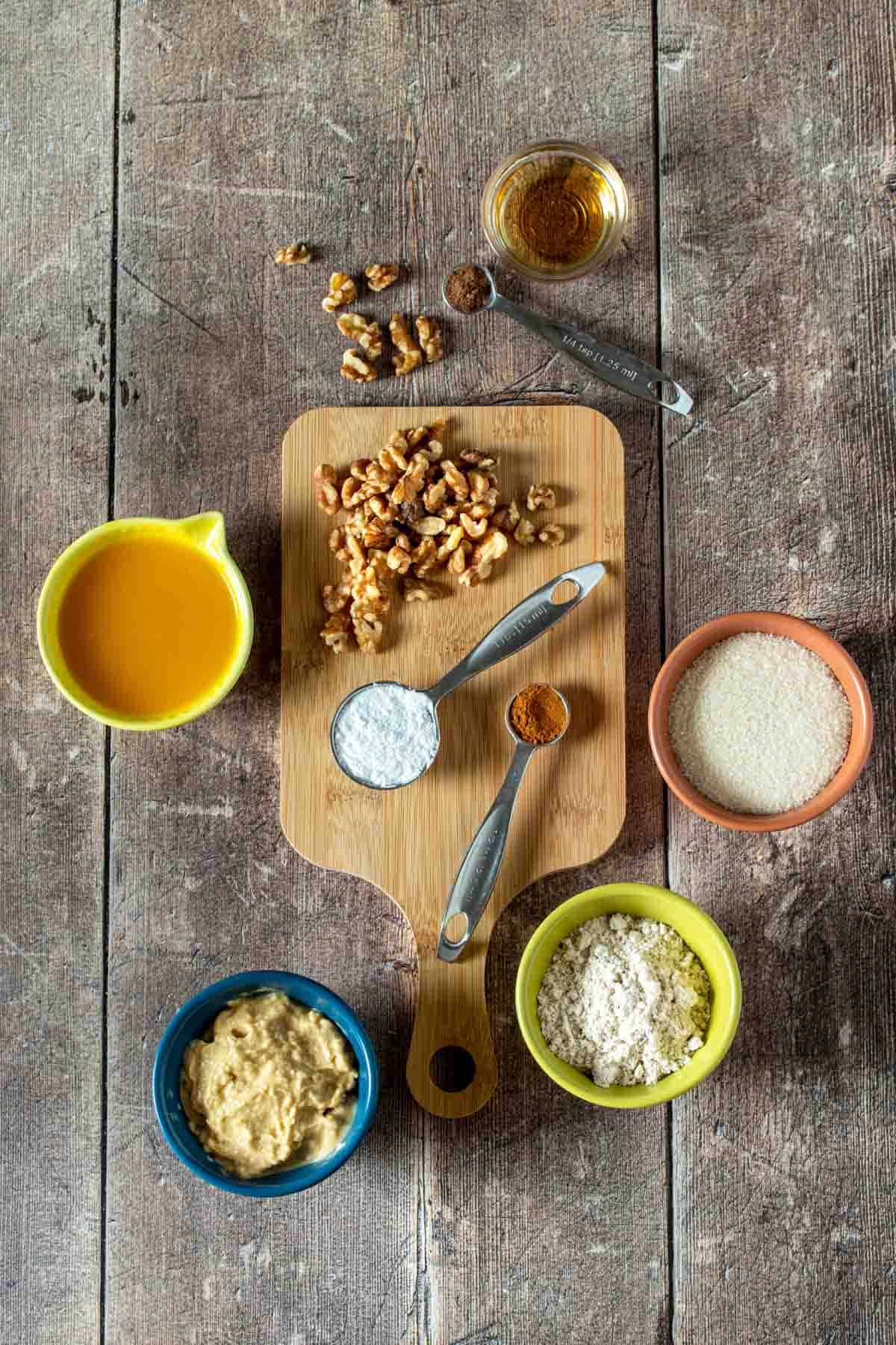 Top view of a wooden surface with bowls of flours, sugar, juice, nuts and spices.