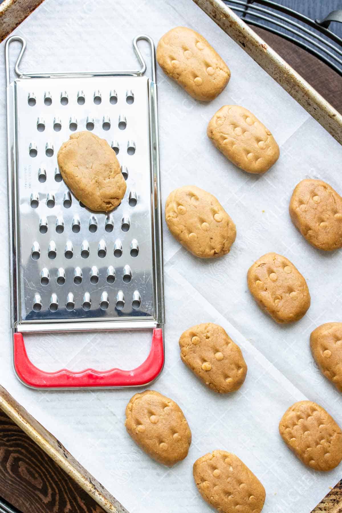 Raw cookies being shaped on a grater and put on a cookie sheet