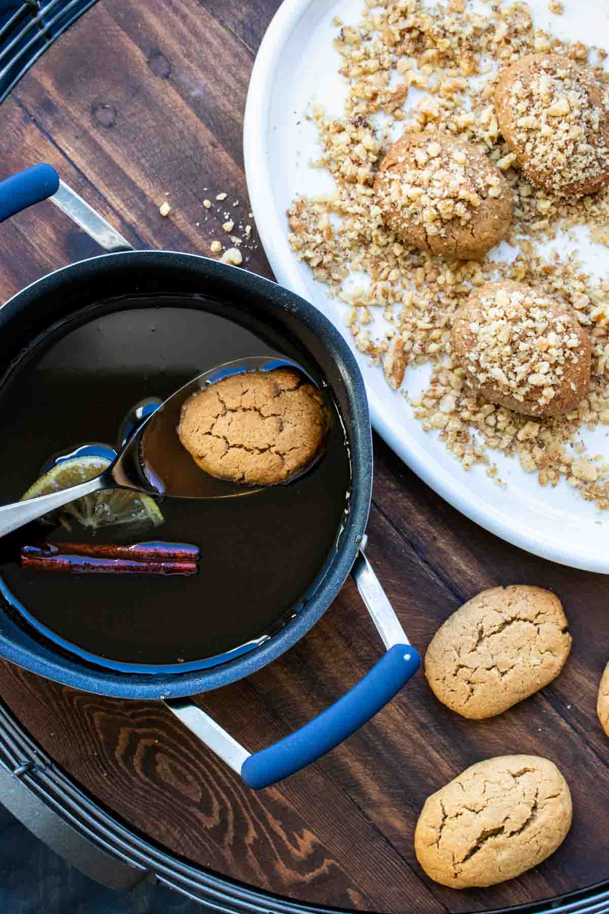 Melomakarona cookie being dipped in a syrup mixture and covered with walnuts