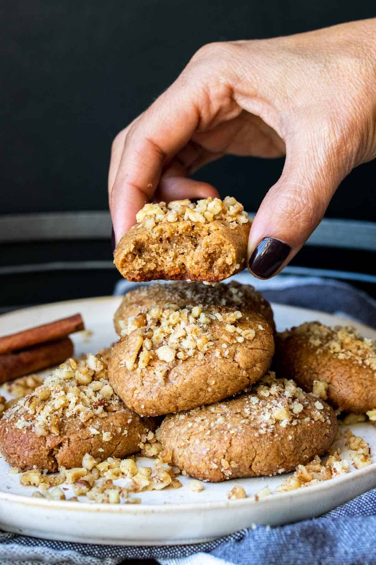 Hand taking a half eaten melomakarona cookie from a pile