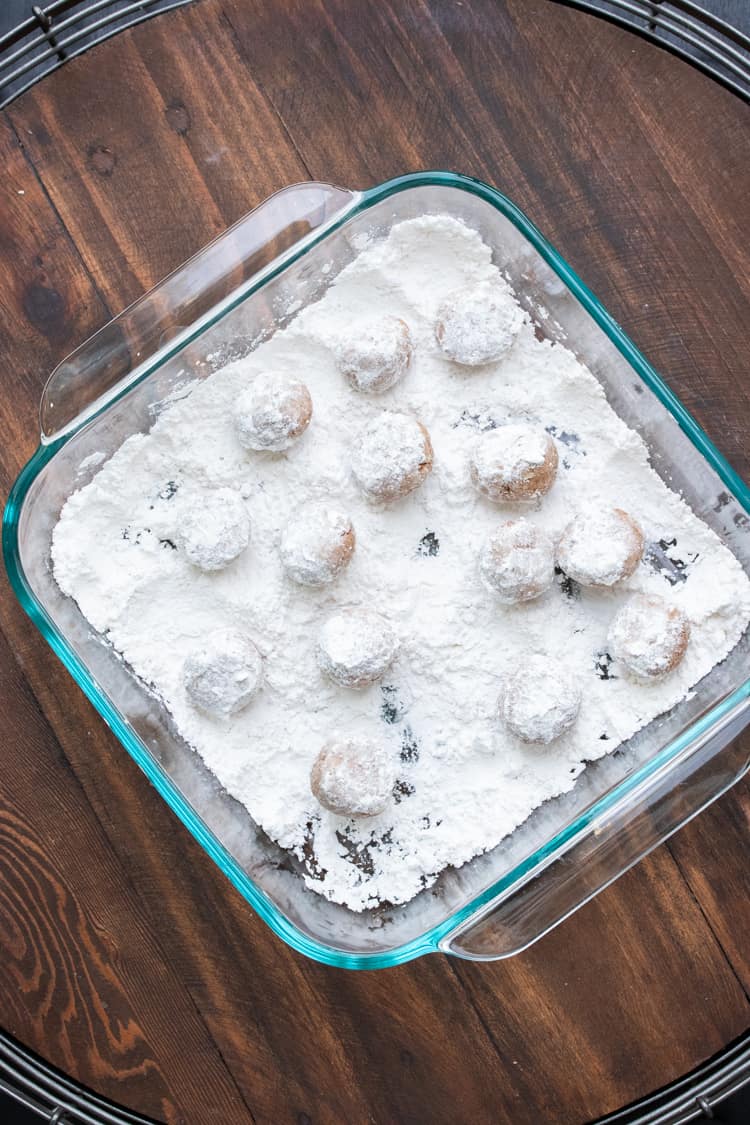 Glass baking dish with cookie balls covered in powdered sugar
