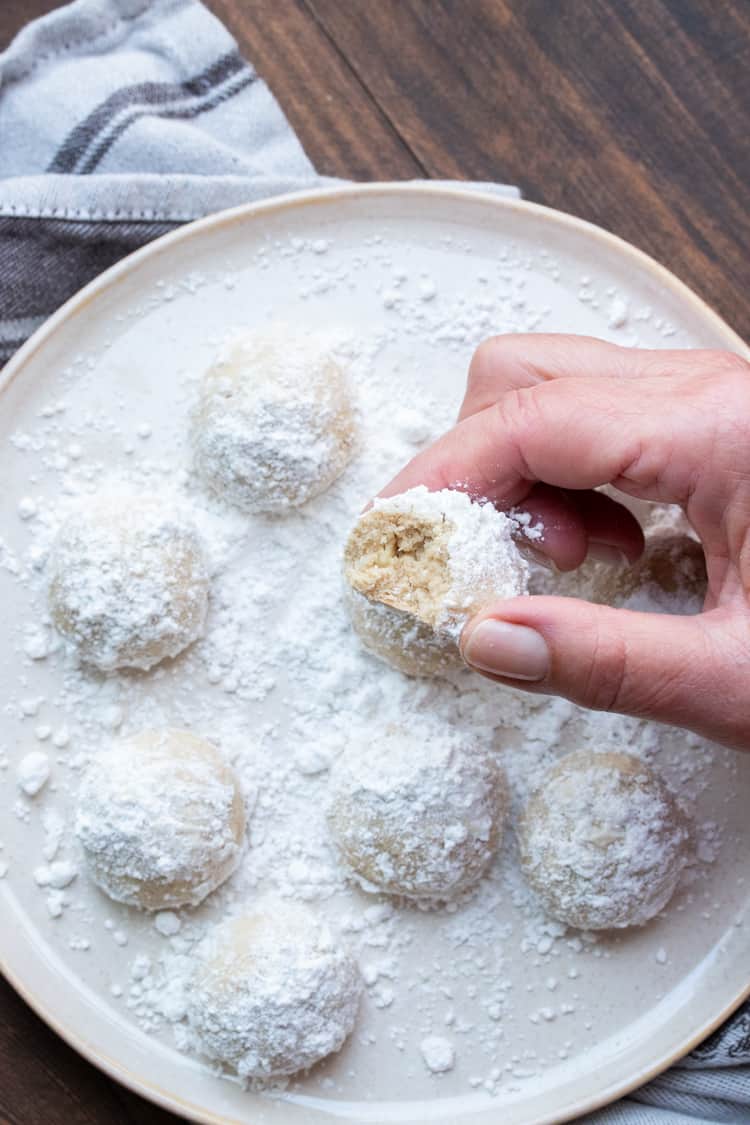 Hand holding a bitten powdered sugar covered butter cookie