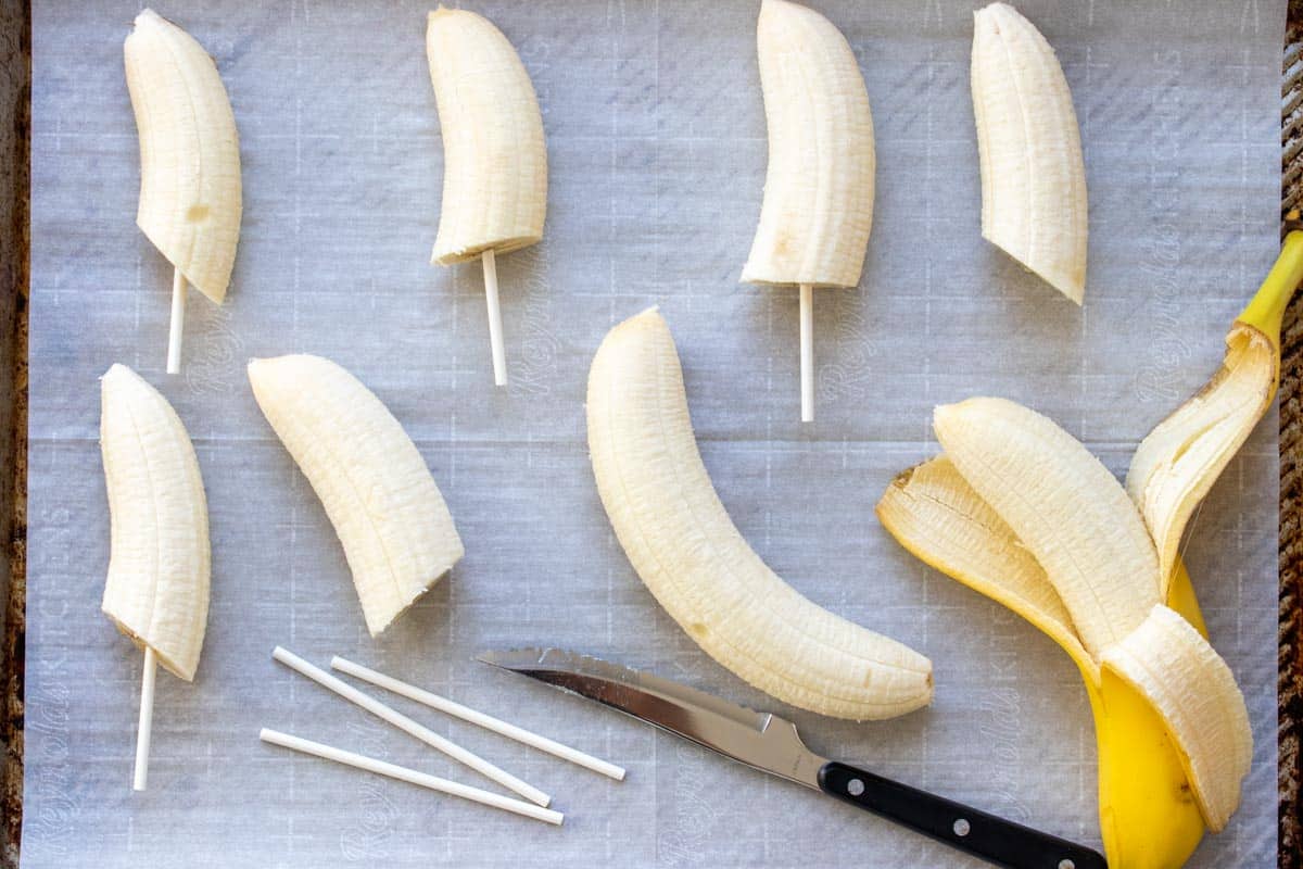 Half cut bananas on sticks laying on parchment paper