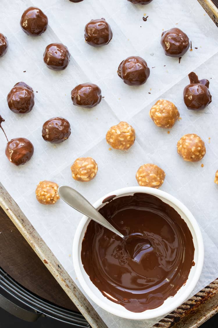 Peanut butter balls being dipped in chocolate and put on a baking sheet