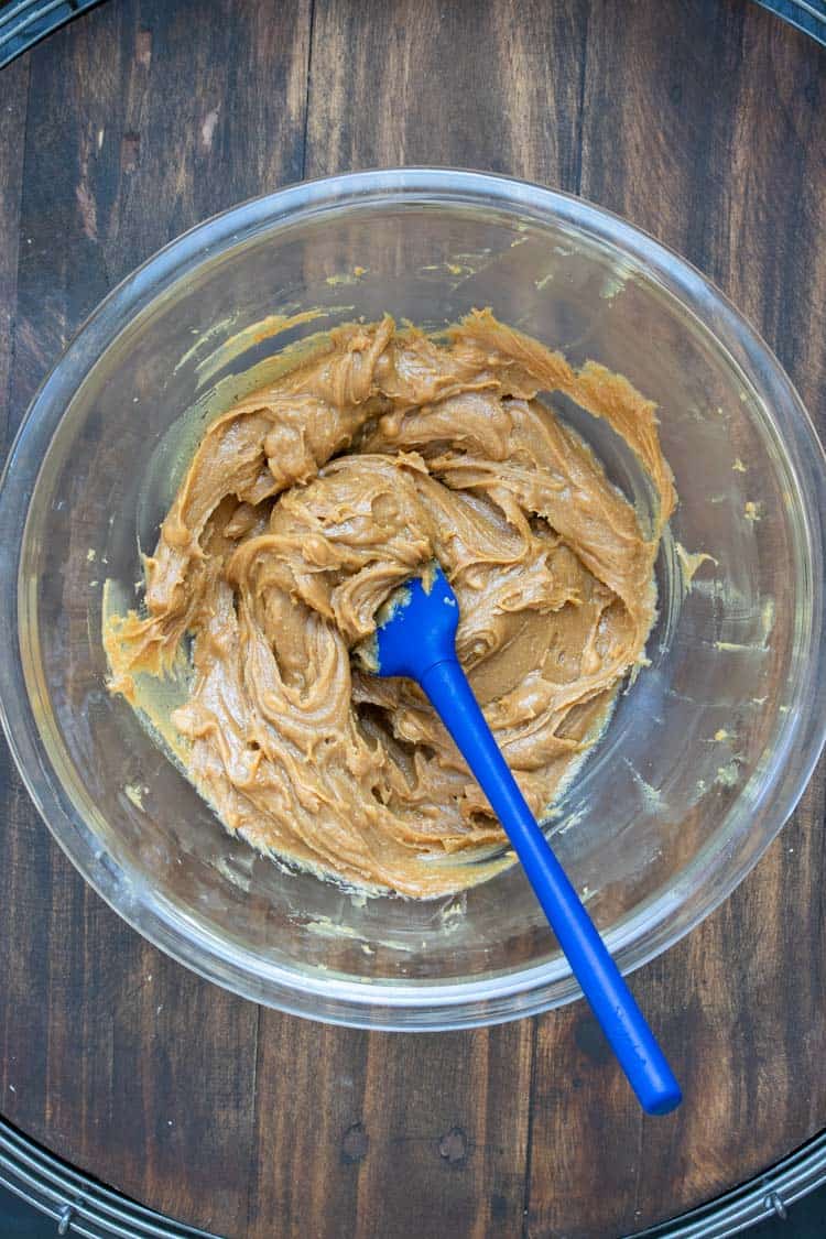 Blue spatula mixing peanut butter in a glass bowl