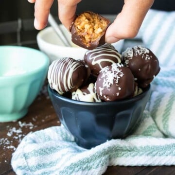 Hand picking up bitten peanut butter ball from a filled bowl of more