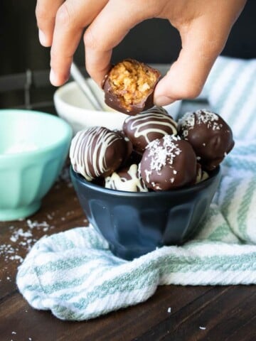 Hand picking up bitten peanut butter ball from a filled bowl of more