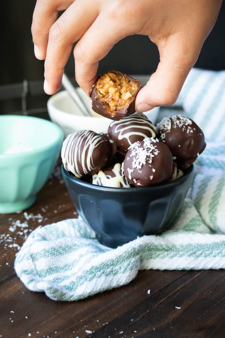 Hand picking up bitten peanut butter ball from a filled bowl of more