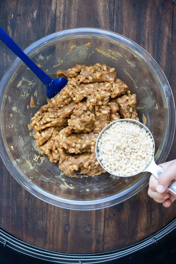 Hand putting crispy rice in a glass bowl with peanut butter