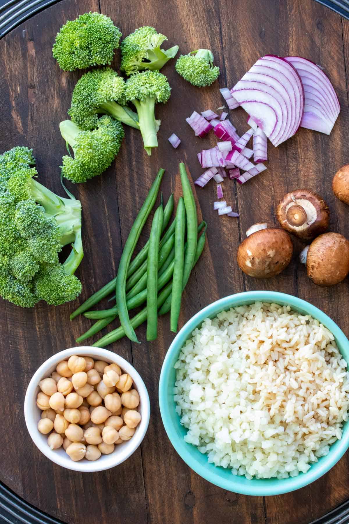 Various veggies laying on a wooden table with bowls of chickpeas and rice