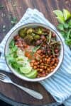 A brown rimmed white bowl with rice, veggies and chickpeas covered in tikka masala sauce