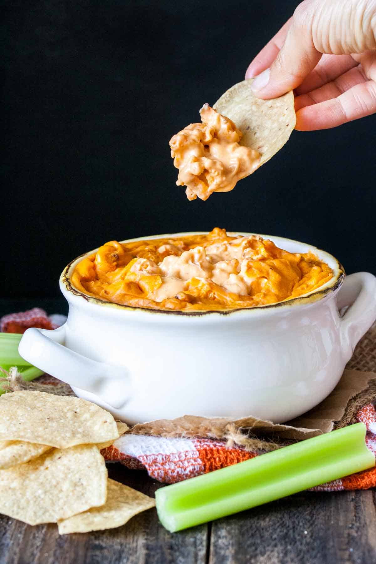 Hand using chip to take a bite from a bowl of baked buffalo dip.