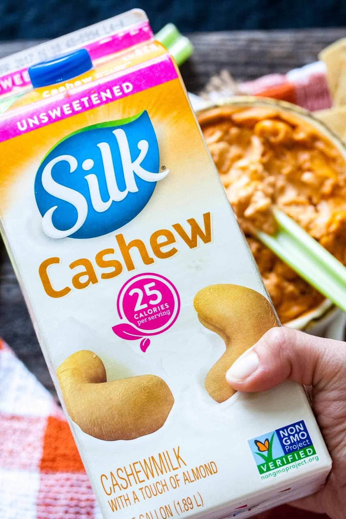 Hand holding a colorful carton of Silk brand unsweetened cashew milk.