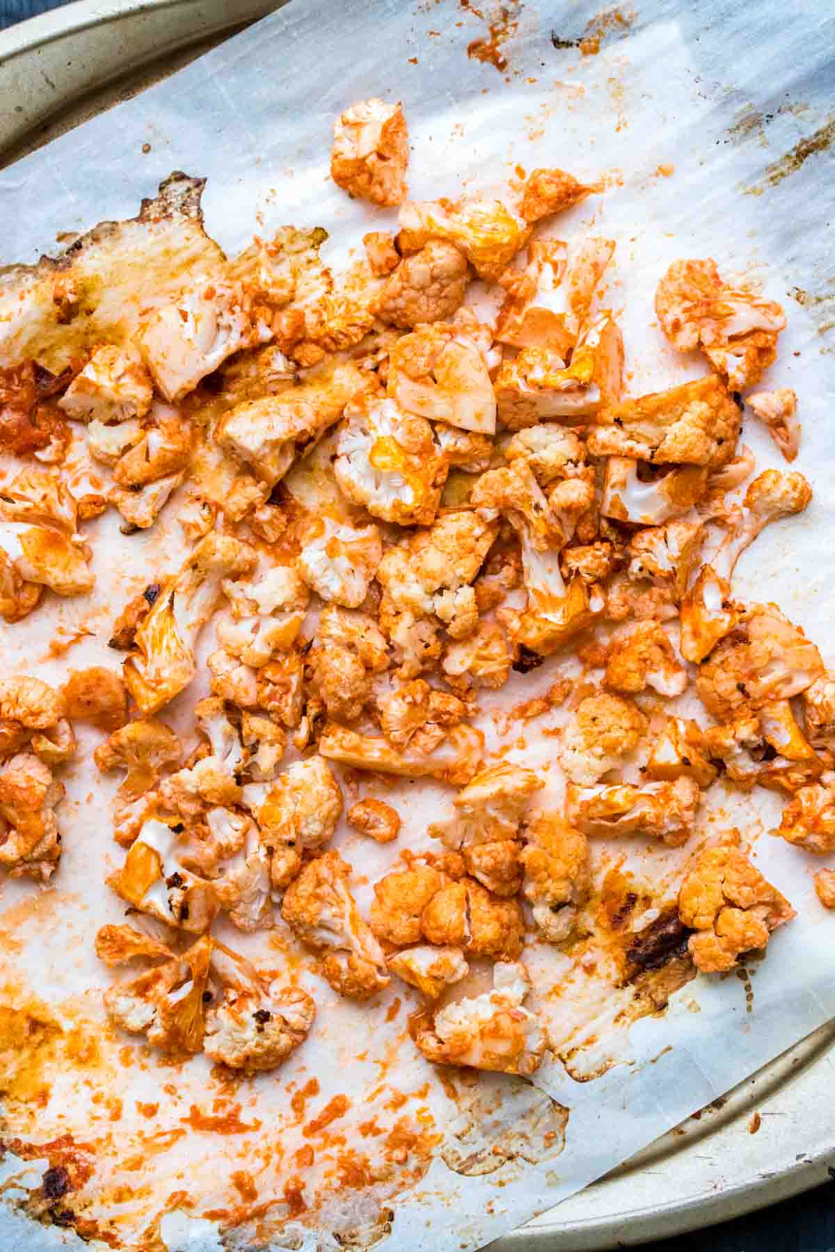 Pieces of cauliflower baked with buffalo sauce on parchment paper