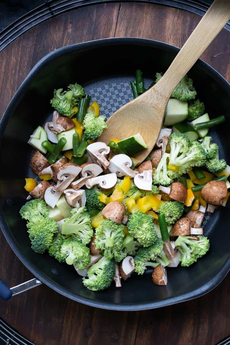 Wooden spoon mixing veggies in a pan