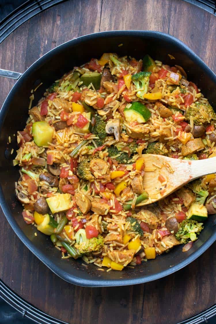 Wooden spoon mixing veggie paella mix in a pan