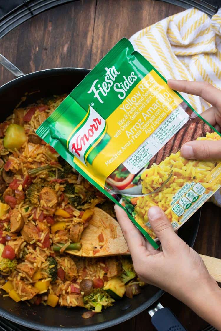 Hands holding package of dry rice mix over a pan of veggie paella