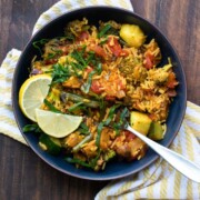 Black bowl of veggie paella topped with lemon slices and strips of greens