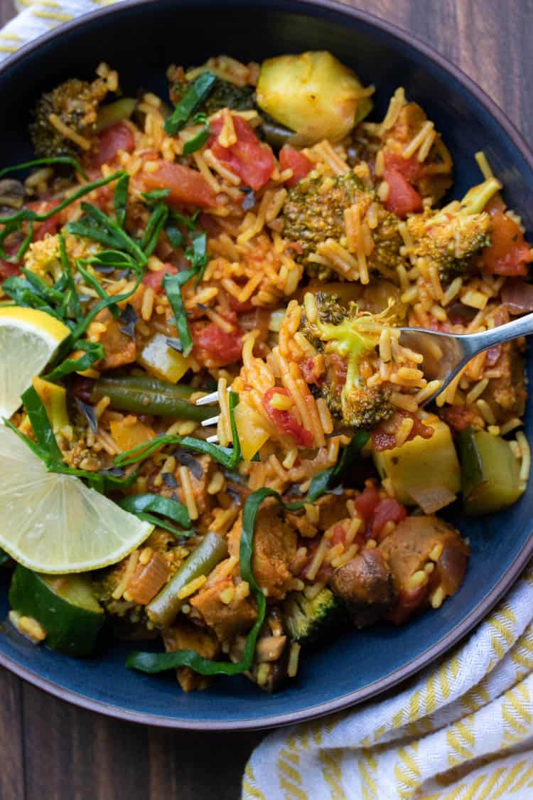 Fork picking up a bite of veggie paella from a black bowl