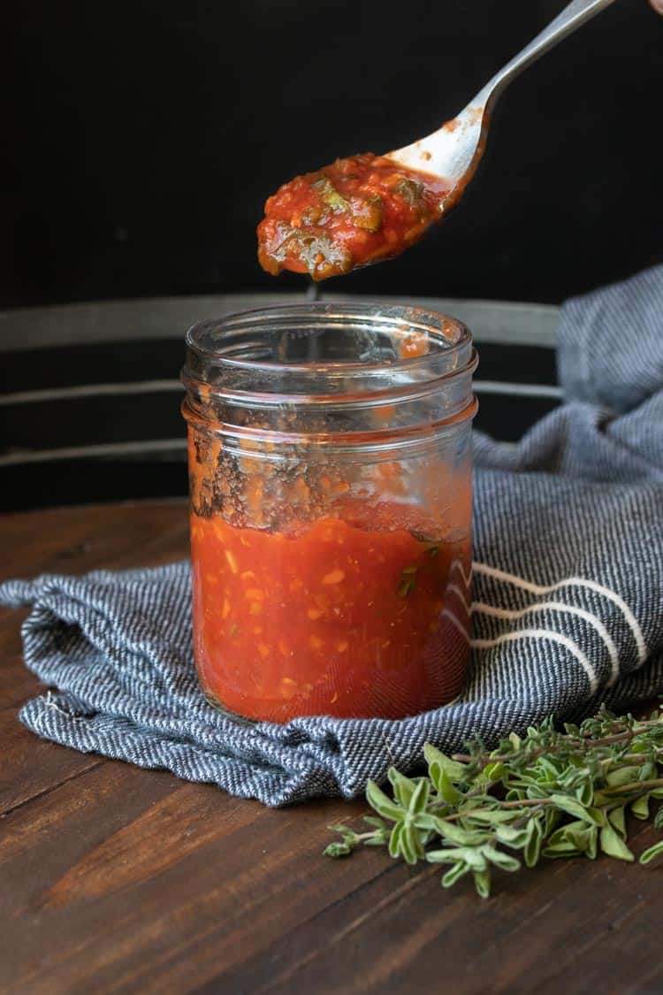 Spoon taking a scoop of tomato sauce out of a glass jar