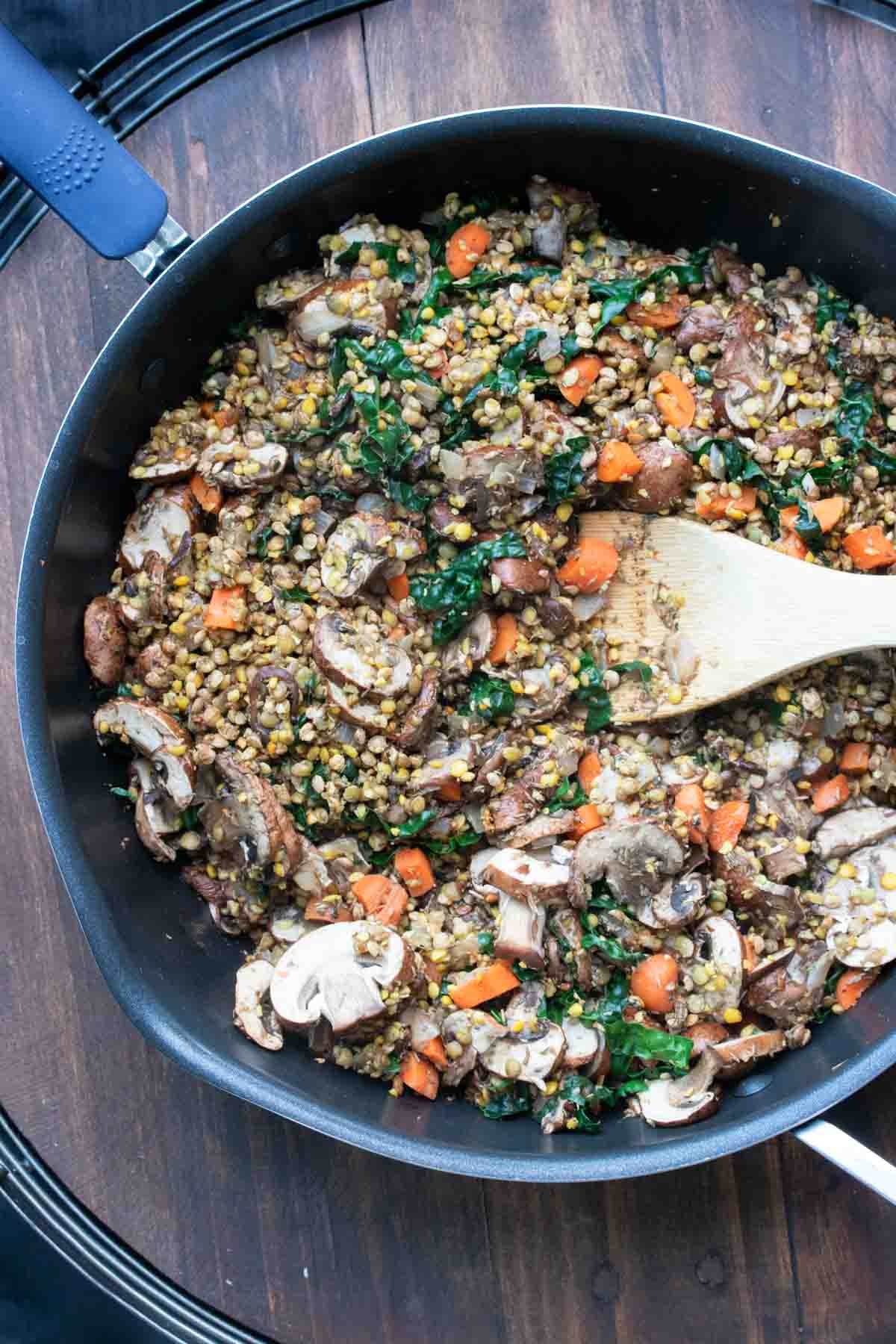 Wooden spoon sautéing lentils and veggies in a black pan.